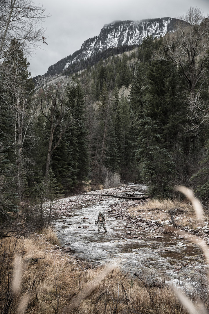 A hunter crosses a frigid high alpine river while bow hunting for elk and other big game.