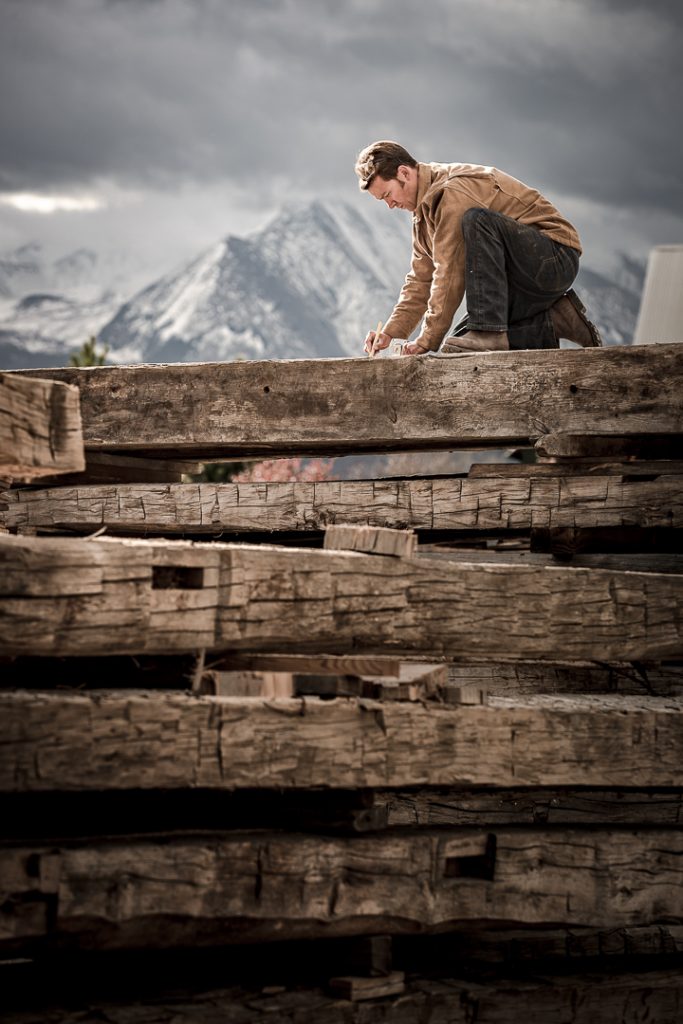 A man makes measurements on a reclaimed beam in Carbondale, Colorado with Mt. Sopris in the background.