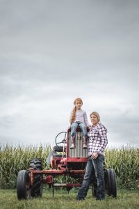 A Woman Farmer and Her Female Daughter Farming On Their Tractor In Their Field.