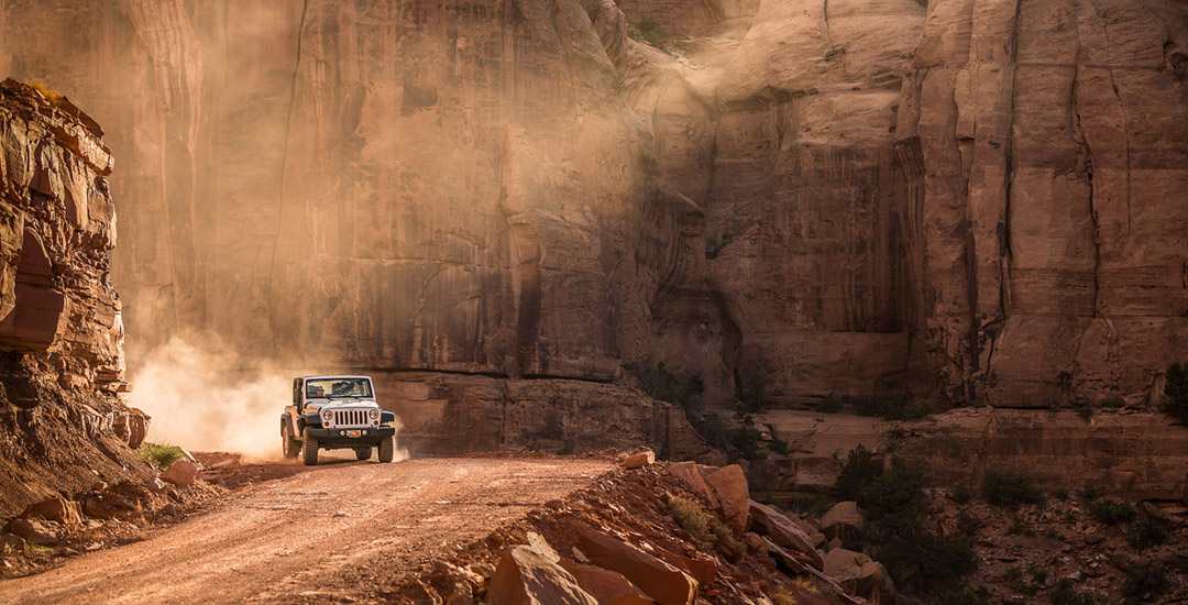 Jeep Wrangler In The Desert Of Moab Utah Driving Down A Dirt Road As The Sun Sets. 