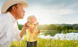 Father Daughter Blowing Flowers In A Field Near Colorado Mountains