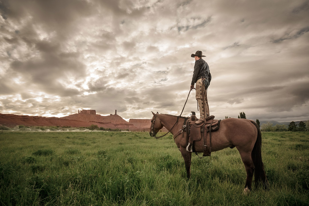 Cowboy Standing On His Horse Surveying The Ranch. 
