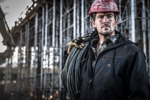 Modern Craftsman Works on a Construction Site while Wearing Heavy Duty Clothing Brands and Safety Gear.