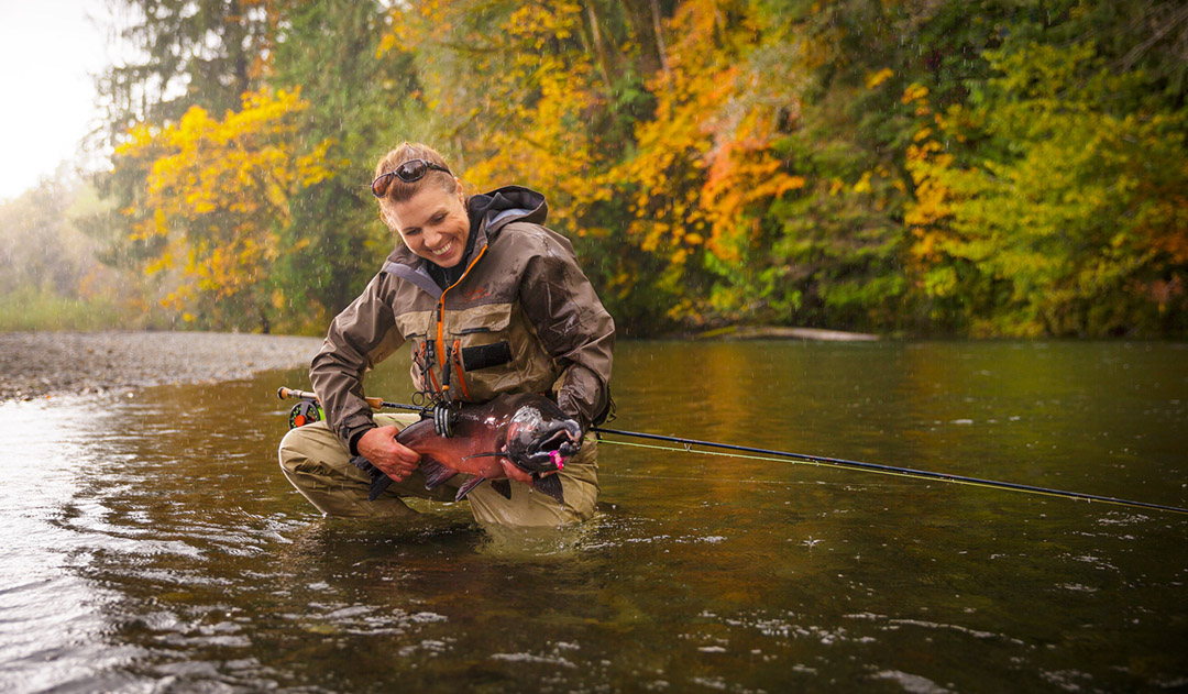 In Clear Cold Water with Fall Colors in the Background, This Triumphant Shot Shows a Woman in Waders with a Cabela's Fly Rod.