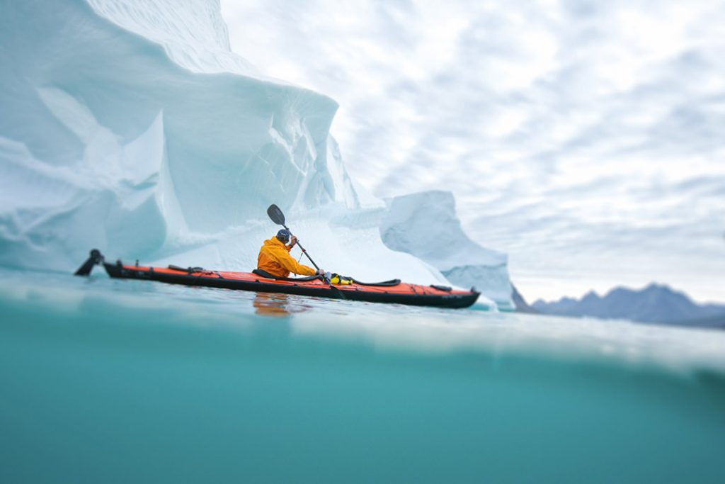 Overseas Adventure Photographer Photographed a Sea Kayaker in Icy Waters near a Tasilaq, Greenland. Blue Water, Fjords, and a Gray Sky Make Dramatic Backdrop.