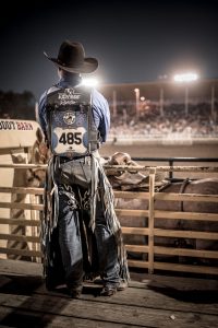 Black Cowboy Hat, Chaps, Cowboy Boots, Spurs, Jeans and Denim Clothing are Worn by a Cowboy Waiting for His Turn at a Bronc Riding Event.