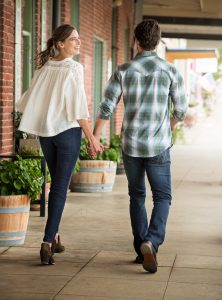 This Couple Walks Hand in Hand Down the Sidewalk of Small Town Mainstreet in Wrangler Brand Casual Apparel.