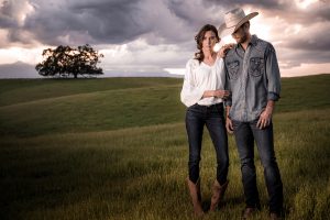 Young Couple Stands In Field Wearing Wrangler Jeans