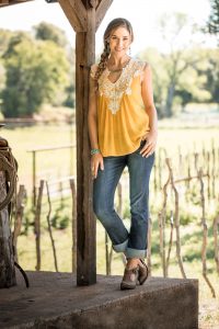 A Lifestyle Portrait of a Young Woman in Western Apparel Posing on a Porch Near a Vineyard.