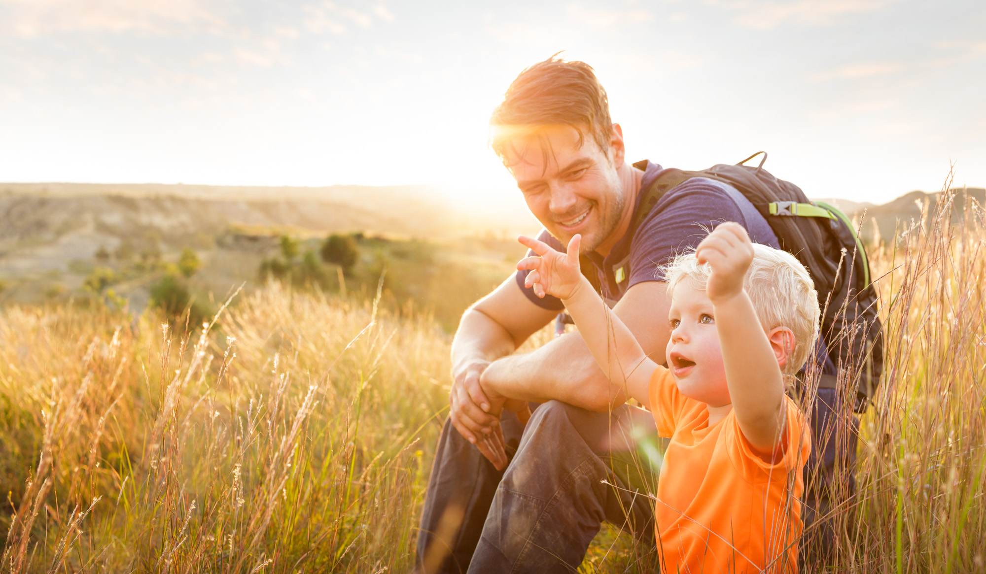 Josh Duhamel sits and smiles at a little boy admiring nature in this sunset photo for North Dakota Tourism, photographed by Tyler Stableford.