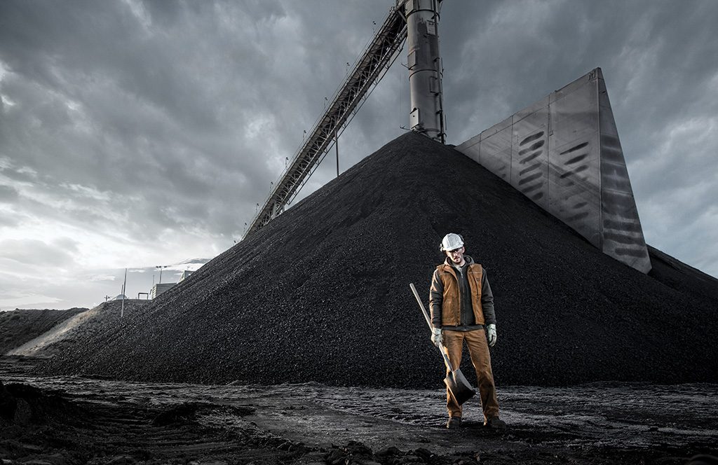 man stands in front of a coal pile at a colorado coal mine. 