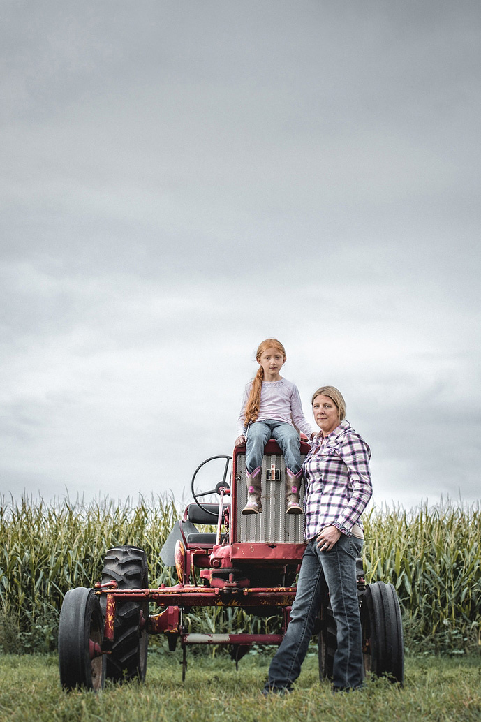 Portrait of mother daughter female farmers with tractor in a corn field.