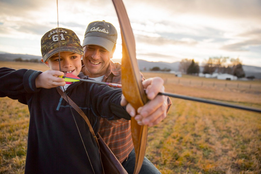 Teaching Hunting Skills to the Next Generation is a Way to Pass On the Outdoor Tradition and This Image of a Father and Son at Sunset Working with a Longbow Captures Those Values.