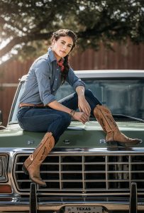 A Wrangler model in denim and cowboy boots sits on the hood of a truck
