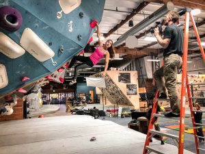 Olympic climber Brooke Raboutou hangs off a hold on a bouldering wall while photographer Tyler Stableford gives her direction.