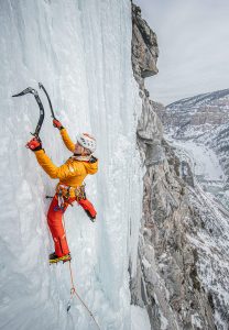 A woman ice climbs high above a Colorado landscape.