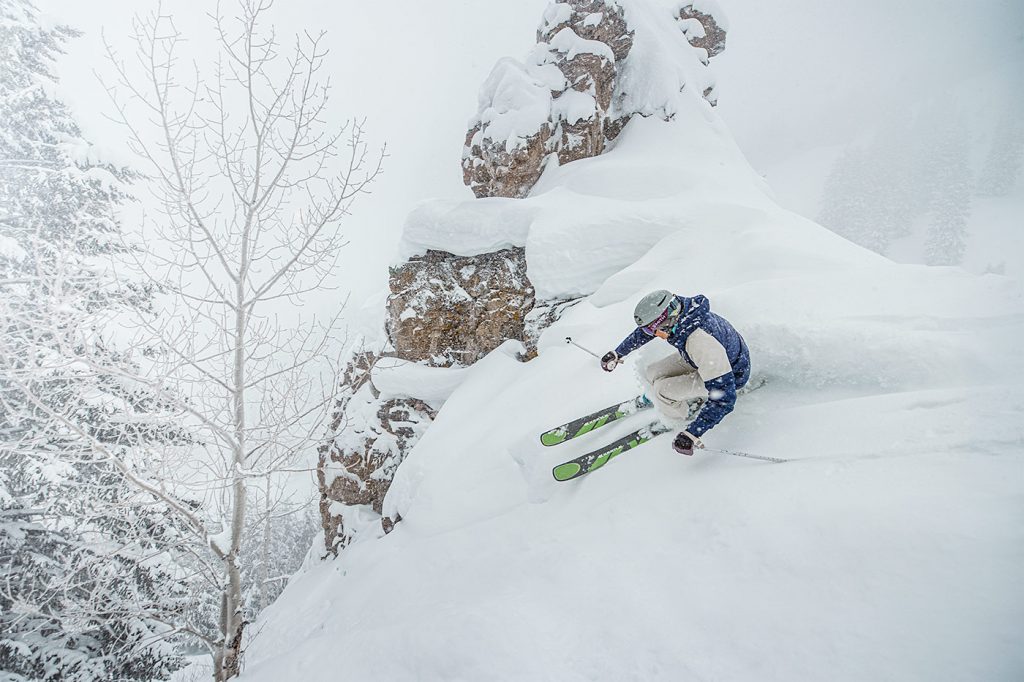 A skier slashes powder by a cliff on Aspen Mountain